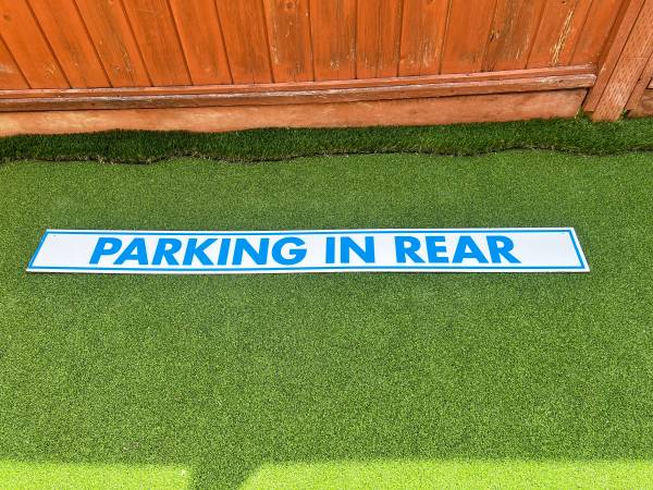 White sign with blue lettering indicating 'PARKING IN REAR', 6’x6” 1